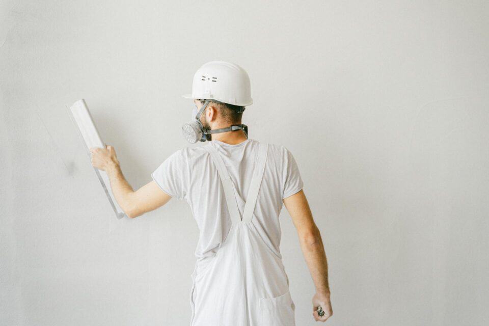 contractor in white coveralls and hard hat smoothing drywall patch