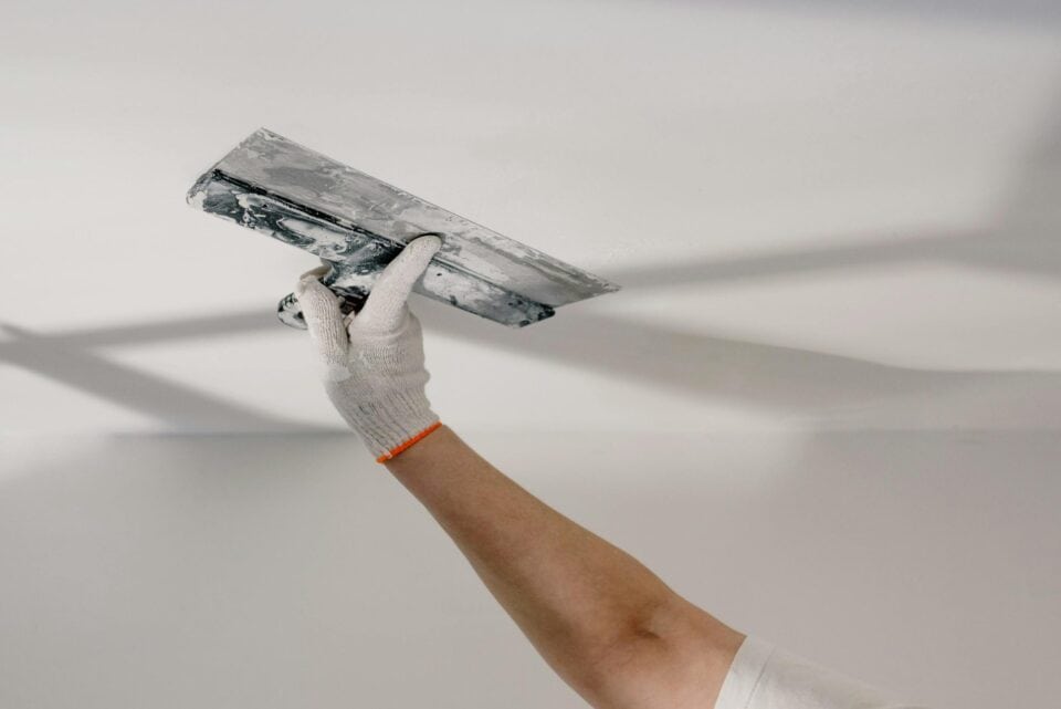 A gloved contractor smoothing new drywall.