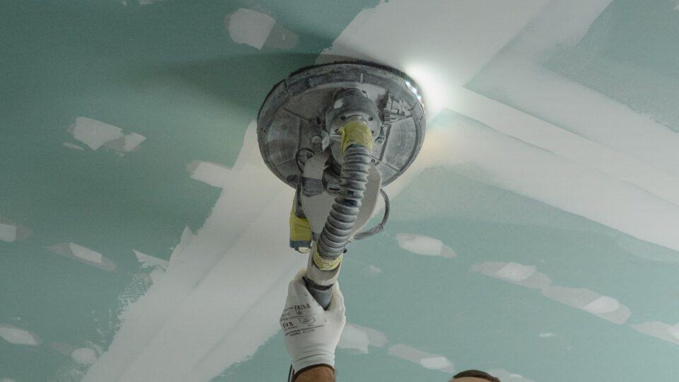 gloved contractor using machine to smooth drywall repair job