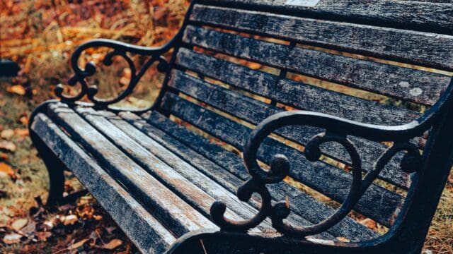An old outdoor bench with black metal legs and worn, black wooden slats.