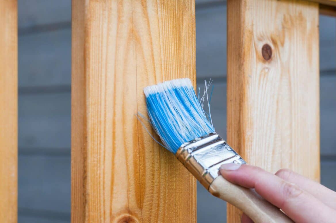 A person holding paint brush applying stain to deck rails.