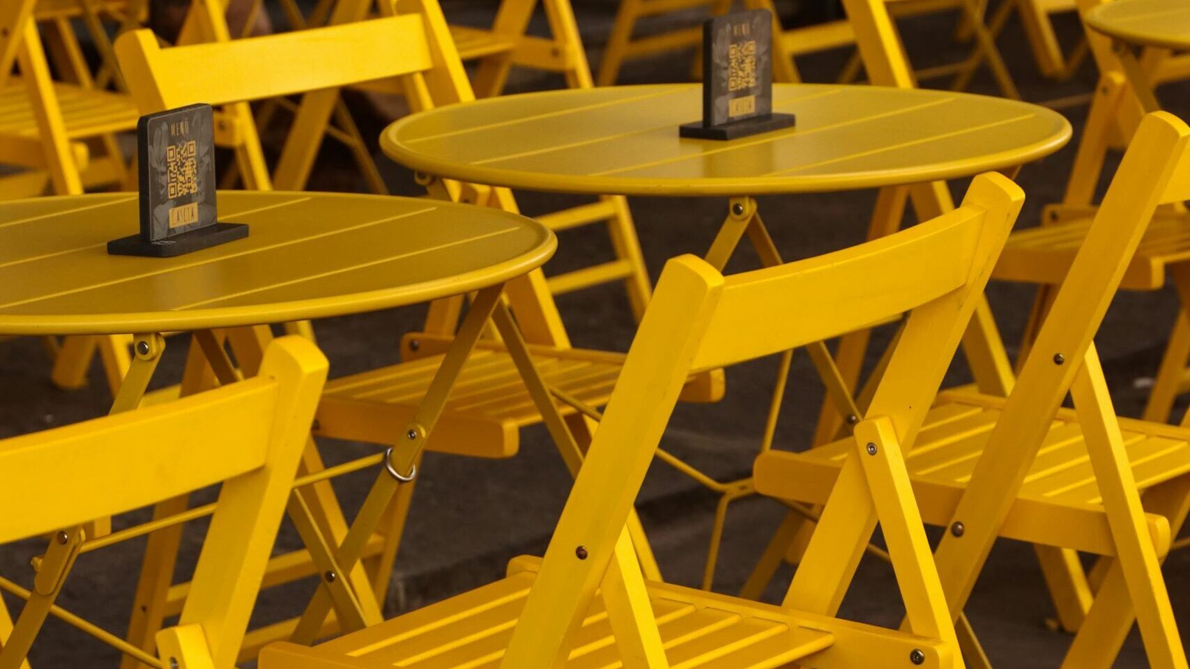 Several rows of yellow painted folding chairs and cafe tables.