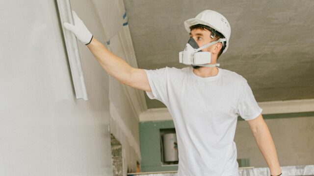 A young man in white hard hat smoothing or repairing drywall.